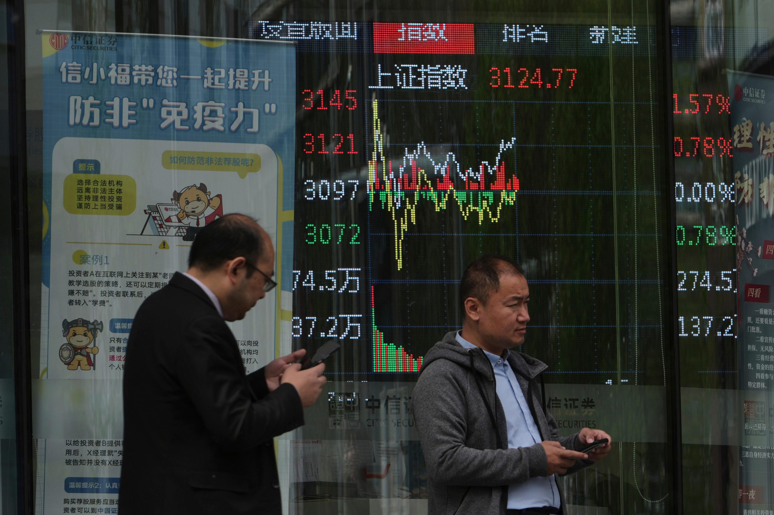 People walk past an electronic board displaying Shanghai shares trading...
